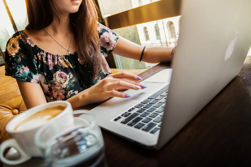 Woman typing on a laptop at a café with coffee